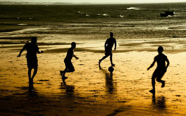 Happy and muscular young man holding soccer ball at beach