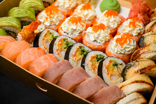 Closeup view on appetizing mix of sushi rolls with salmon, avocado, smocked eel, tobiko caviar in delivery box. Takeaway order. Delivery food.