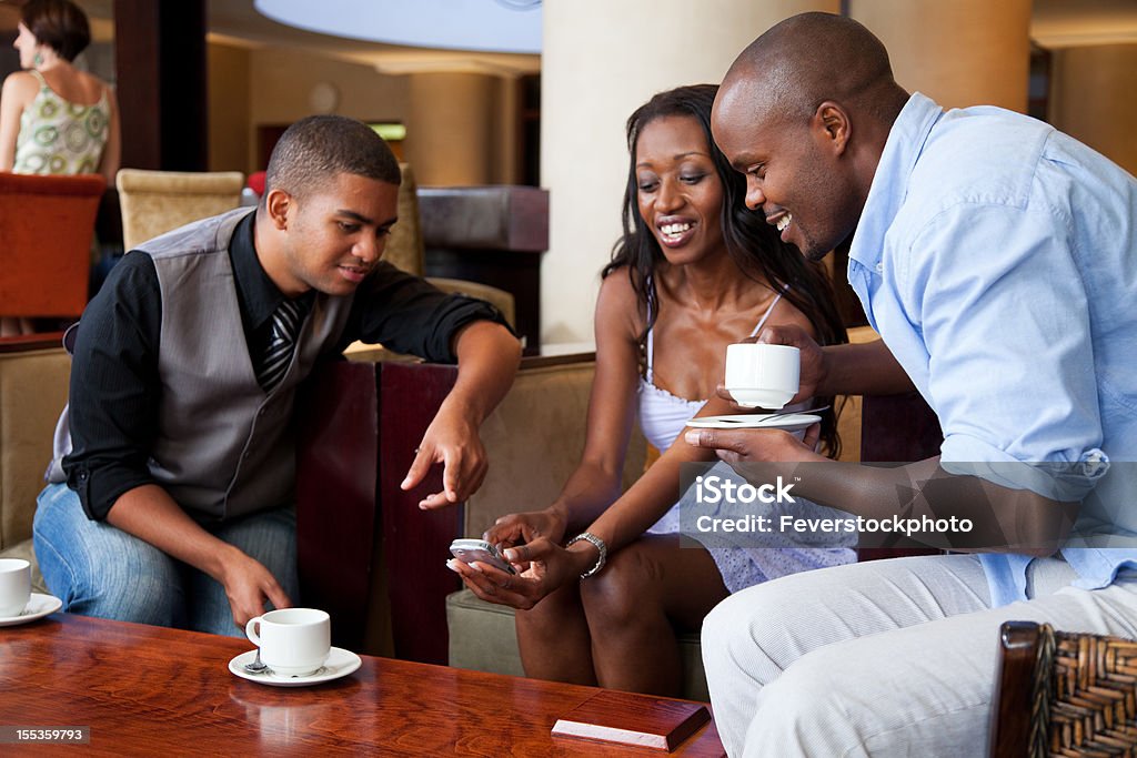 Amici nel Lounge con un caffè e guardando il telefono cellulare - Foto stock royalty-free di Accogliente