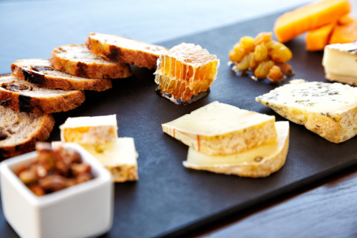 Fancy cheese plate with blue cheese, cheddar, goat cheese, bread, honey and pistachios at a luxury restaurant.  Horizontal shot. High angle view.