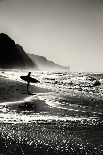 Surfer on the Beach Photo of a surfer looking at the sea in the Magoito Beach in Sintra, Portugal. Black and white, film and grain simulation on processing. black and white beach stock pictures, royalty-free photos & images