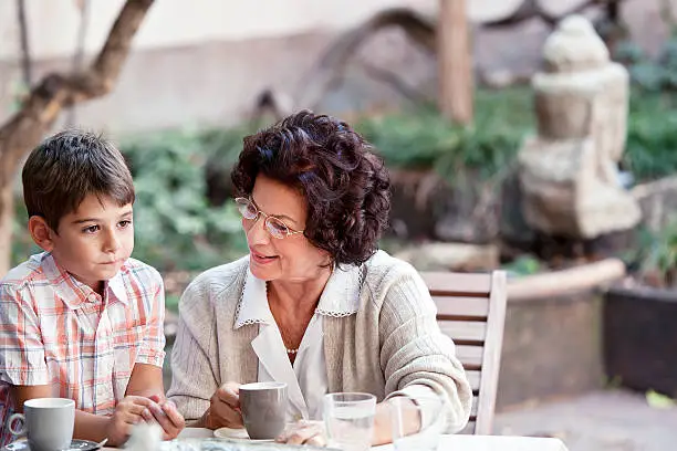Grandmother is talking to her grandson at the coffee table. Copy space. See more of this family: