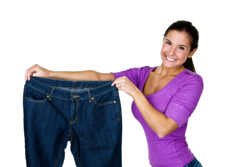 Cute young woman holding up a pair of oversize jeans for a weight loss concept