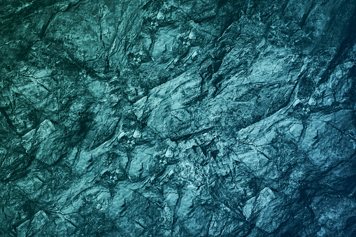 Blue green gray teal aqua turquoise rough mountain surface. Close-up. Toned stone rock mineral granite texture background. Cracked, crumbled. Underwater, water or ice, frost effect.Color gradient.Dark