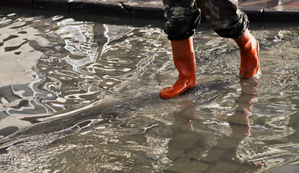 Waterproof trouser and rain gumboots to protect two legs of a man stands on the flooded road in severe weather cyclone raining afternoon