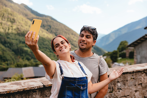 Young couple taking a selfie with mobile phone while doing rural tourism in a mountain village. Holiday trip and outdoor summer vacation in Huesca, Spain