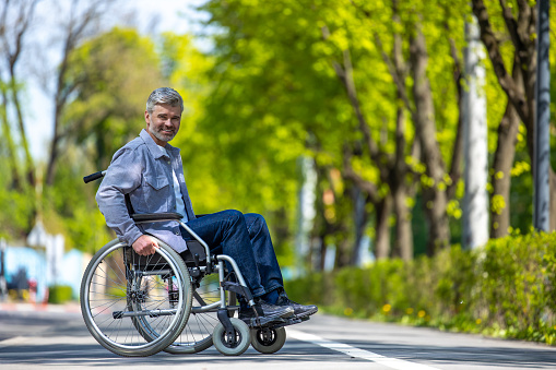 Handicapped man in wheelchair wearing casual clothing riding on street road, outdoor leisure for disable guy.