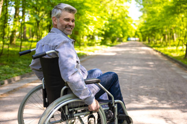 istock Gray haired disable man in wheelchair spending free time in park. 1553614714