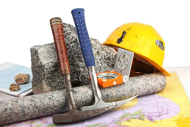 Geological fieldwork tools: geological hammer, compass, granite drill core, hardhat, rock samples, and geological maps.
