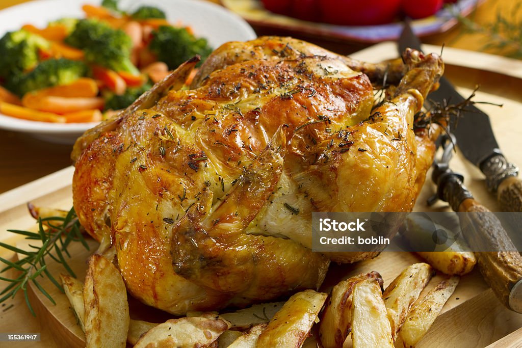 Roast chicken dinner, topped with thyme Whole roasted chicken on a cutting board seasoned with fresh rosemary, served with roasted potatoes, and garden fresh carrots and broccoli. Roast Chicken Stock Photo