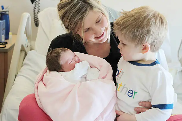 Photo of Mother Holding Newborn Baby and Toddler in Hospital