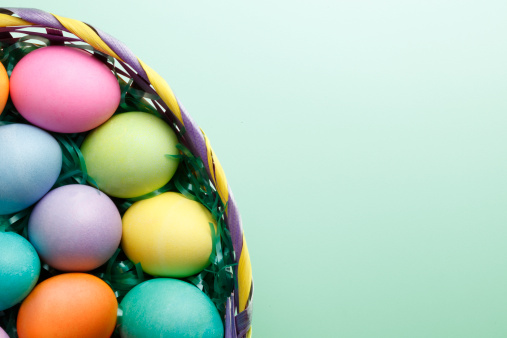 A top view of Easter eggs in an Easter basket on a pastel green background.