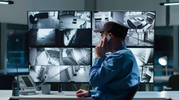 istock Security officer answer phone call watching cctv cameras on multi-screen workstation 1553623650