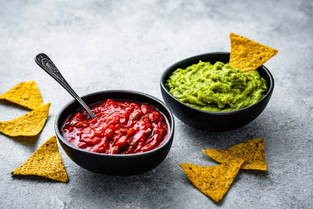 Bowls of salsa sauce and guacamole with nacho chips on gray background