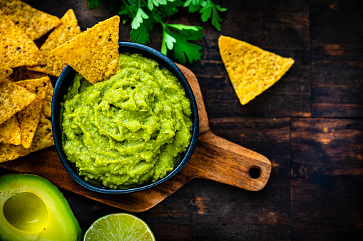 Mexican food: guacamole and nachos shot from above on dark wooden table.. High resolution 42Mp studio digital capture taken with Sony A7rII and Sony FE 90mm f2.8 macro G OSS lens