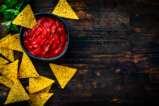 Salsa sauce and nacho chips shot from above on dark wooden table. Copy space at the right. High resolution 42Mp studio digital capture taken with Sony A7rII and Sony FE 90mm f2.8 macro G OSS lens