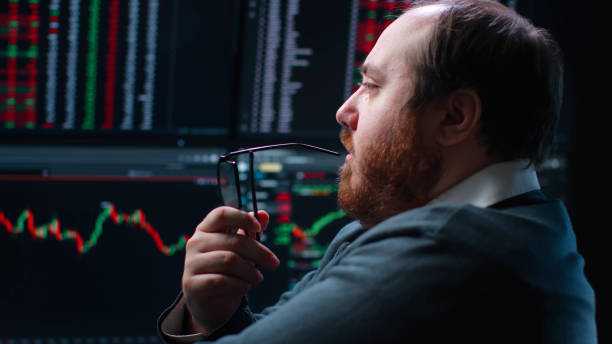 istock Close up of pensive fat trader look at multiple computer screens with data 1553627002