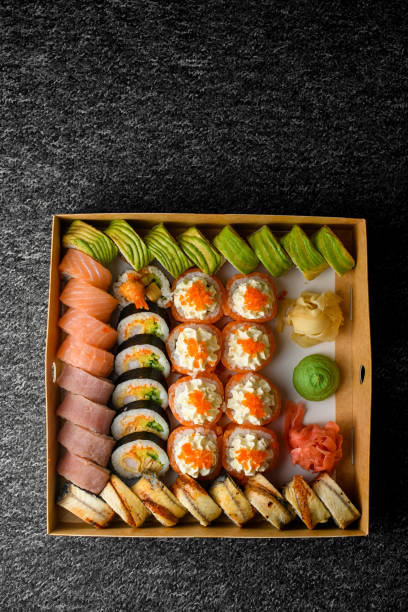istock Top view on different sushi rolls with salmon, avocado ,smocked eel in delivery box on black carpet 1553630002