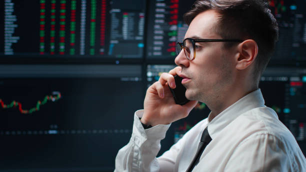 istock Stock market broker talking on mobile phone with graphs on multiple computer screens at background 1553635682