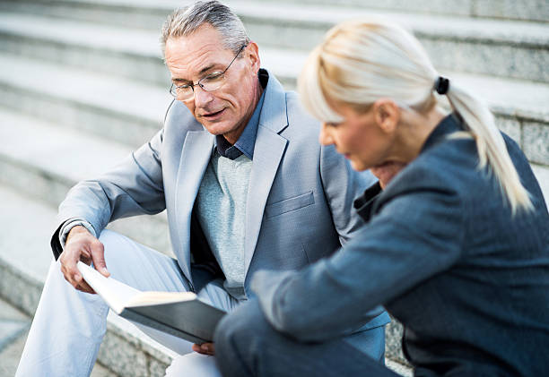 istock Two businesspeople sitting on stairs and looking at notebook. 155364125