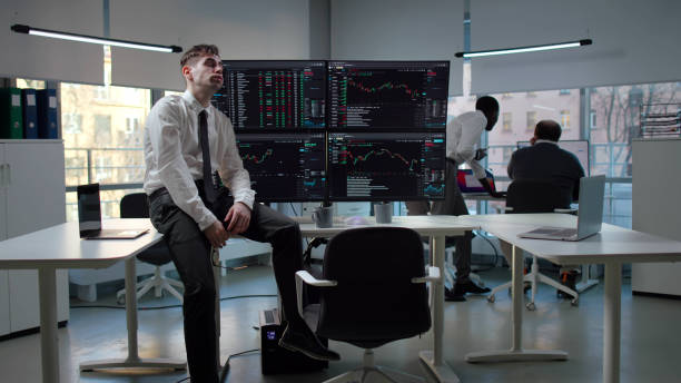 istock Tired and stressed trader sitting at desk with multiple computer monitors in office 1553648234
