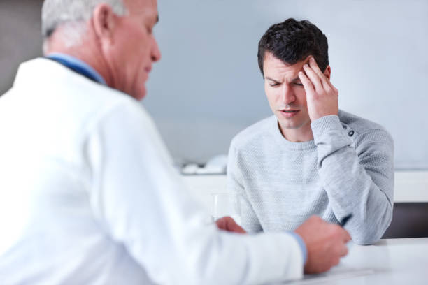 "Thanks, Doc" Young man rubbing his forehead in agony while his doctor is writing out a prescription doctor head stock pictures, royalty-free photos & images