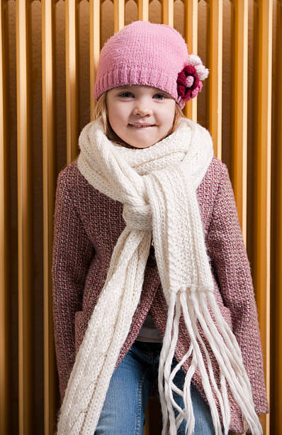 portrait of cheerful child girl in white winter warm hat and scarf sending blowing a kiss air isolated on blue background