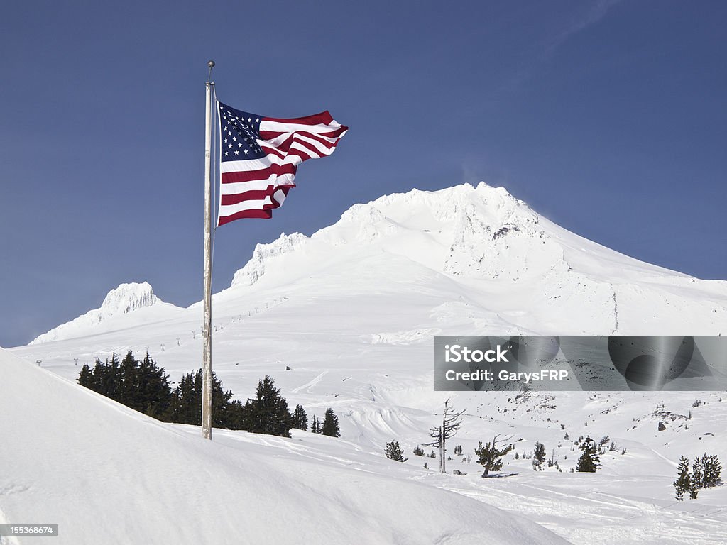 Mount Hood Peak US Flag Blue Sky at Timberline Oregon A United States Flag blowing in the wind near the Wy'East Day Lodge across from Timberline Lodge. Summit of Mt Hood ( South Side ) located in Northwest Oregon. Taken of a sunny Spring like day. This photo is located near Timberline Lodge, a National Historic Landmark and has the top of a ski lift visible. Flag Stock Photo