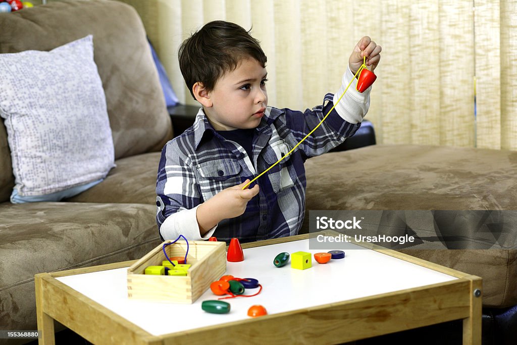 Boy threading a string of beads Young boy developing good fine motor skills as he tries to thread multi-colored beads on a string. Child Stock Photo