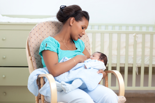 Mother breastfeeding a newborn baby, seating on rocking chair at baby room.