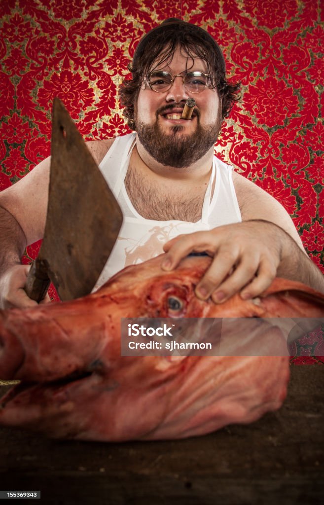 Butcher Cutting Pig's Head with Rusty Cleaver, Smiling This creepy butcher is using a rusty cleaver to butcher a pig's head. He's wearing a too-small hat, glasses, a white undershirt, and a white apron. He holds a cigar in his mouth. Death Stock Photo