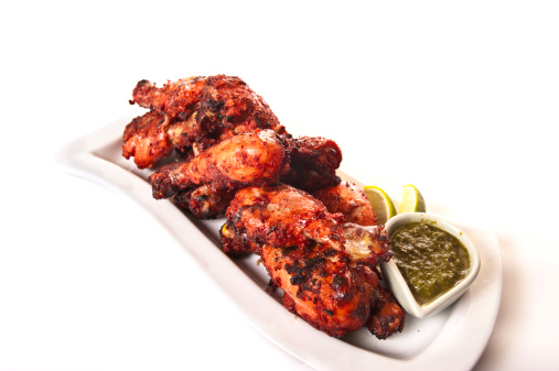 A plate of tandoori chicken drumsticks served with chutney and lime slices.