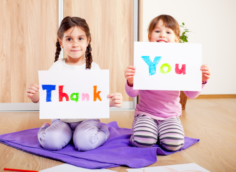 Two little girls showing colorful THANK YOU message on white papers.