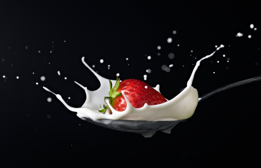 fresh strawberry splashing into spoon full of milk