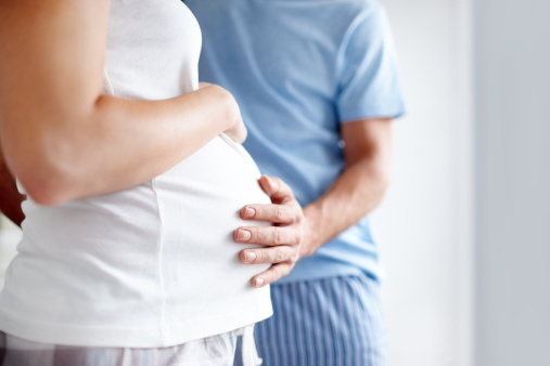 Side view of a pregnant woman holding her belly as the husband touches it affectionately