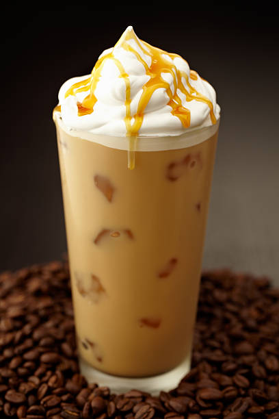 Iced coffee with cream and caramel on top and coffee beans around base of glass, shot with very shallow focus on cream.  Professionally color corrected, exported 16 bit depth, retouched and saved for maximum image quality.