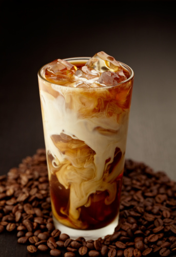 Iced coffee with cream swirling down through the ice and coffee beans at base of glass, shot with very shallow focus.  Professionally color corrected, exported 16 bit depth, retouched and saved for maximum image quality.