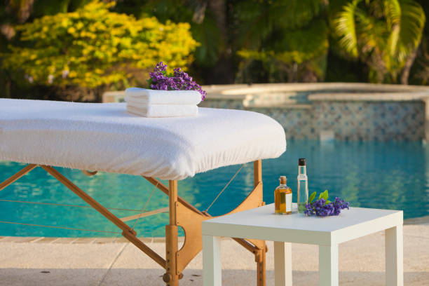 Spa Massage table with massage oils and towels by pool side early in the morning massage table stock pictures, royalty-free photos & images