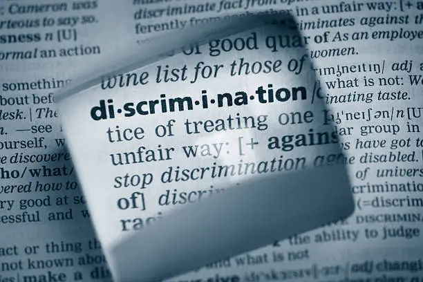 The Dictionary definition of the word “discrimination” photo taken through magnifying glass from a page of a dictionary with selective focus.