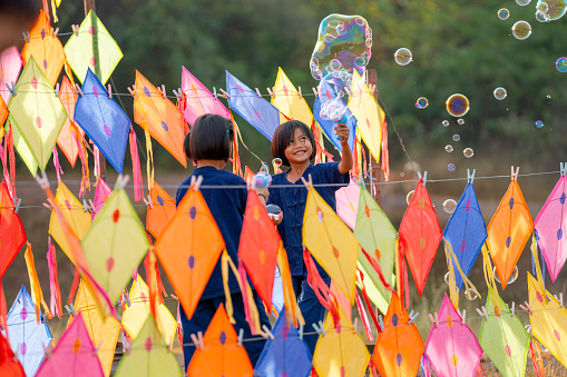Close up of two Asian girls enjoy to play with bubble that create from bubble gun and happy playing with friends in area of many kites.
