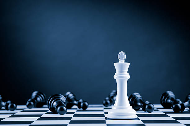 White Chess King among lying down black pawns on chessboard stock photo