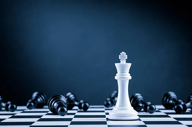 Photo of White Chess King among lying down black pawns on chessboard