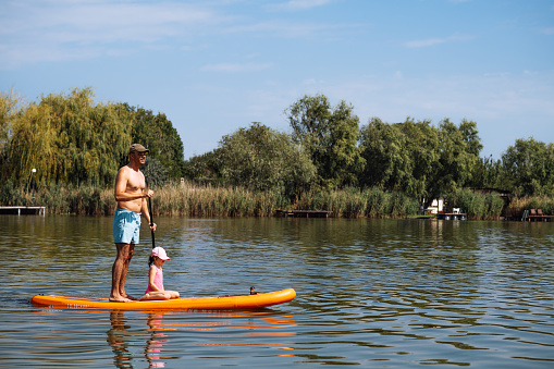 Father and preschool girl on stand up paddle board