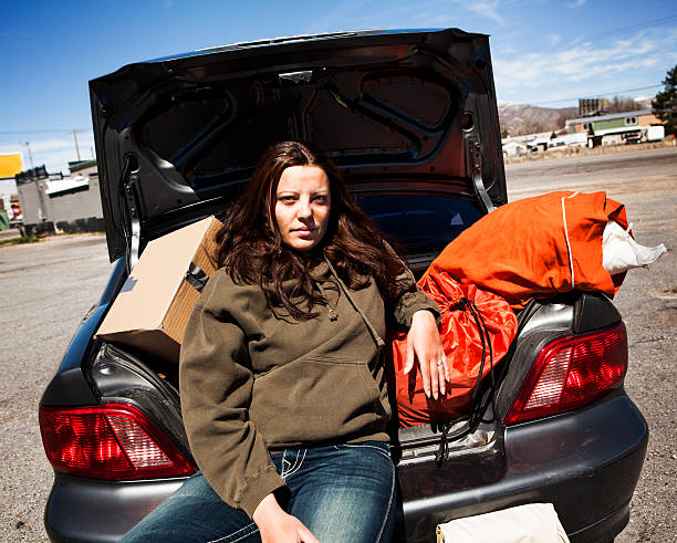 Sans-abri femme assise à l'arrière de la voiture avec effets personnels - Photo