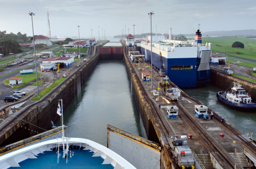 A cruise liner approaching the first of the Panama Canal Locks, Gatun Lock, early in the morning, with the lock gates just opening to allow entry into the first lock. A cargo vessel is in the second parallel lock. Both vessel are heading West towards the Pacific Ocean