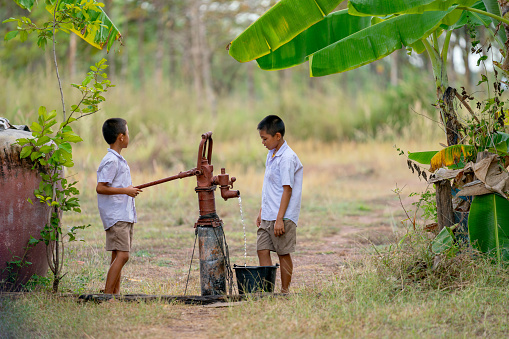 Two Asian boys use groundwater lever to get water for clean and also to grow some plants in the field.