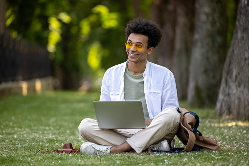 Digital nomad. Young curly-haired man working on laptop in the park