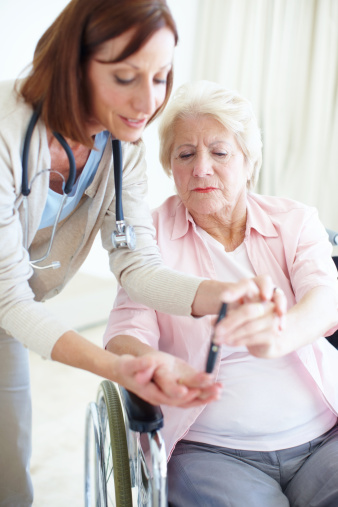 A caring nurse helps an elderly female patient check her blood sugar levels herself