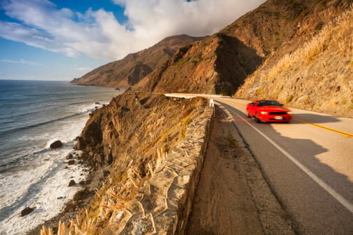 Car drives by the Pacific ocean rocky beach coast in California on the Cabrillo highway US 1