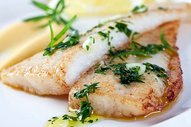 Closeup photograph of white fish Fillet of white fish with parsley, garlic, olive oil and lemon sauce. bass fish stock pictures, royalty-free photos & images